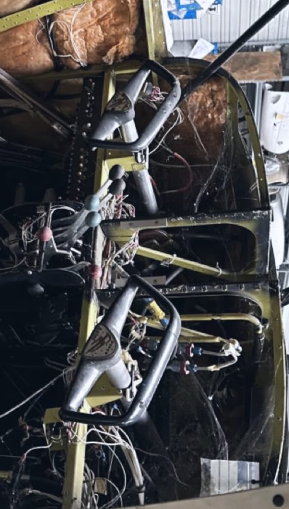 Interior of a partially stripped aircraft cockpit with exposed wiring and bare airframe ribs.