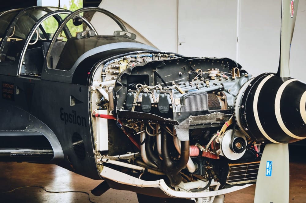 A Socata Epsilon trainer in a hangar with its engine exposed, parts ready for recovery.