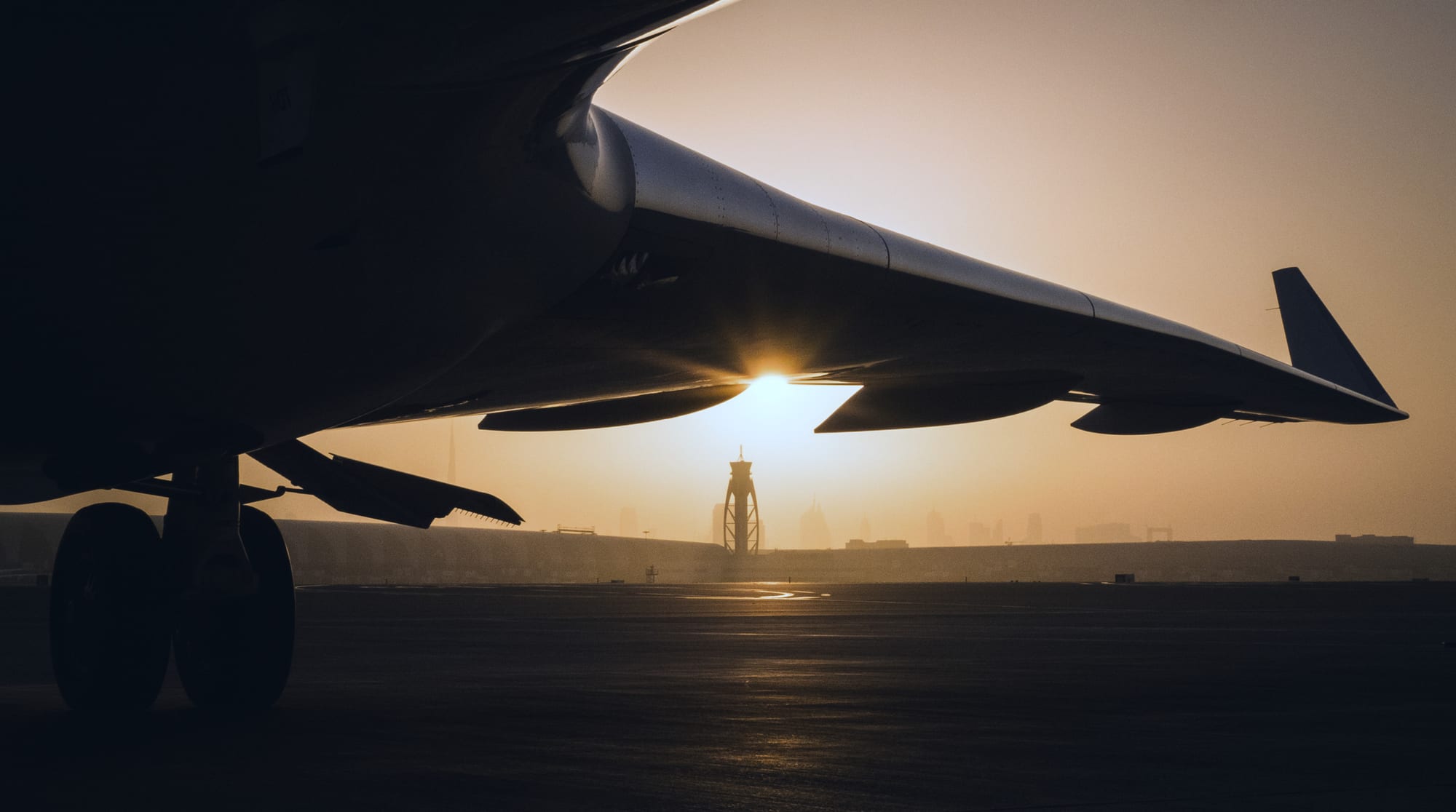 An aircraft wing and landing gear silhouetted on the apron at sunrise
